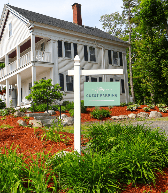 A sign indicating "Guest Parking" near a charming white house surrounded by greenery and mulch.