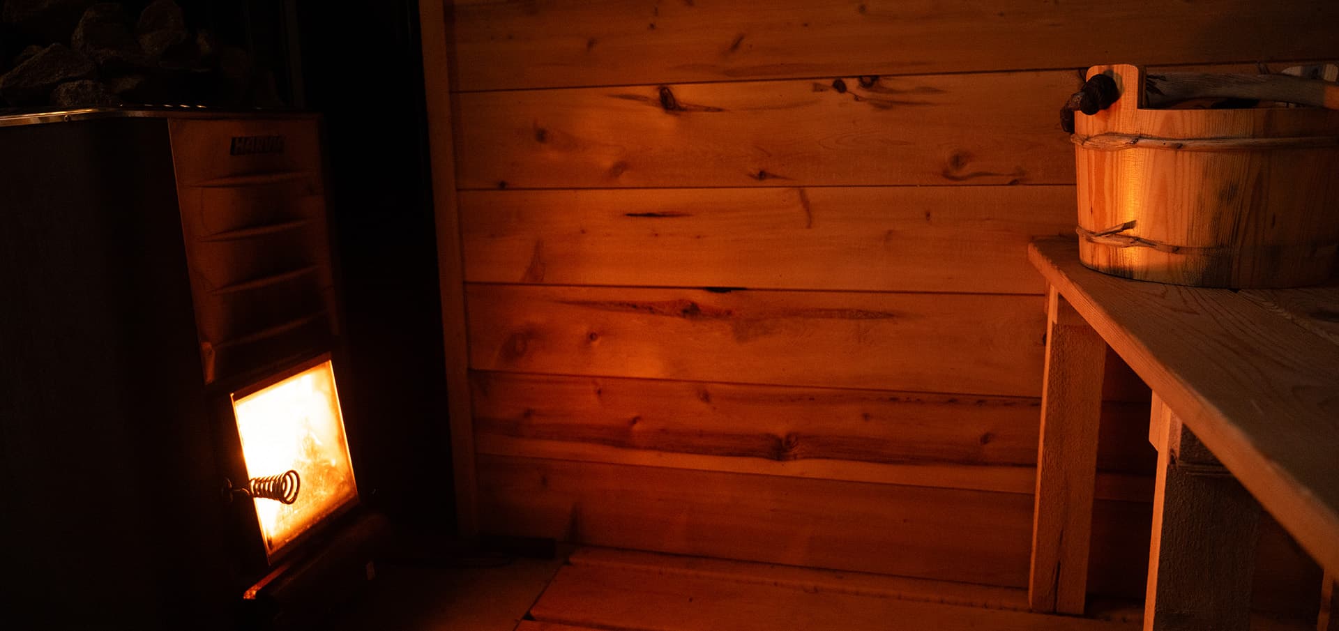 Interior of a rustic cabin with a glowing stove and wooden walls.