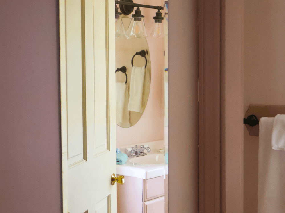 View of a bathroom through an open door, featuring a sink, mirror, and towels.