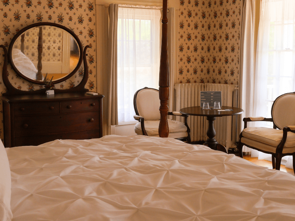 A cozy bedroom featuring a plush bed, vintage furniture, and floral wallpaper.