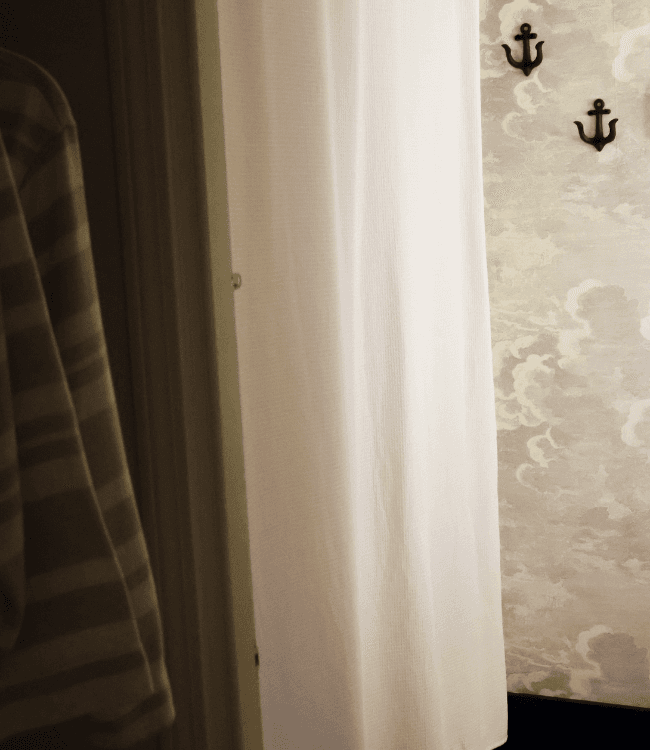 A white curtain partially conceals a room with cloud-patterned wallpaper and wall hooks.