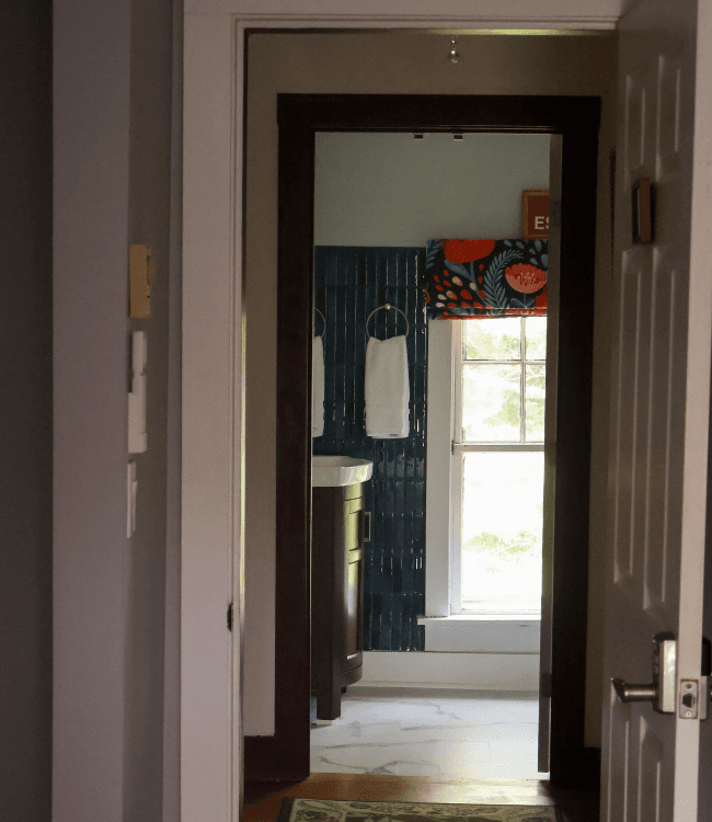 View of a hallway leading to a bright bathroom with towels and a patterned window treatment.