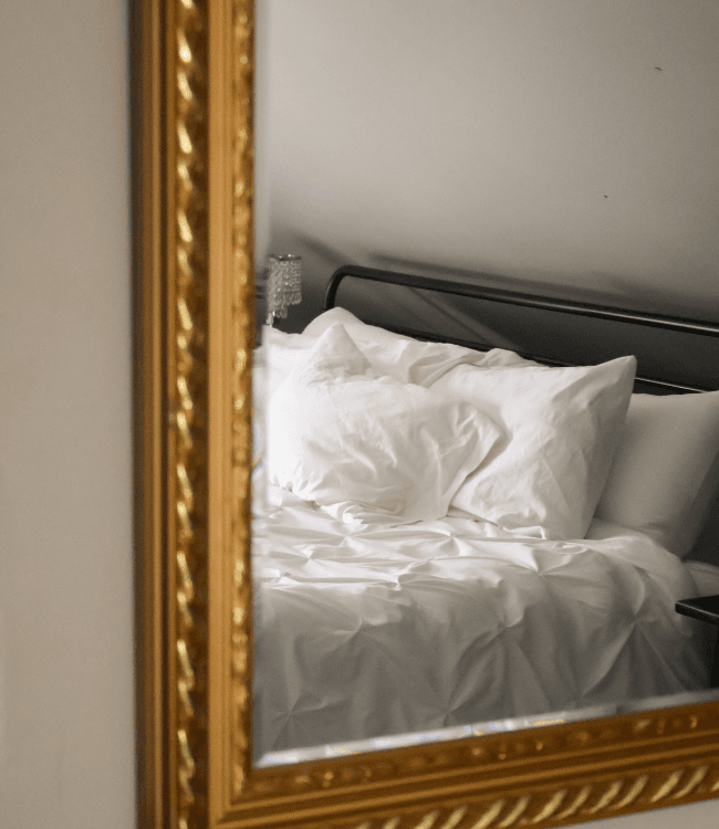 A luxurious bedroom reflected in an ornate mirror, featuring a neatly made bed with white linens.