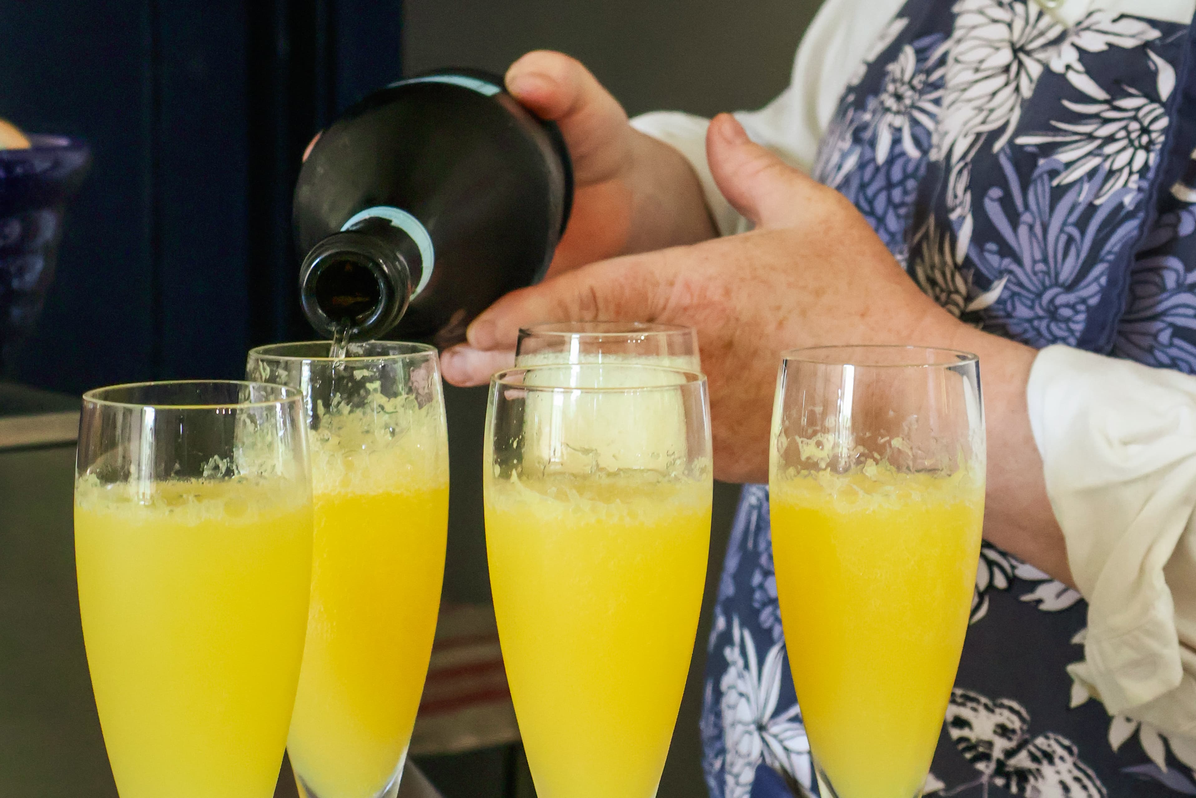 A person pours sparkling wine into glasses filled with orange juice to make mimosas.
