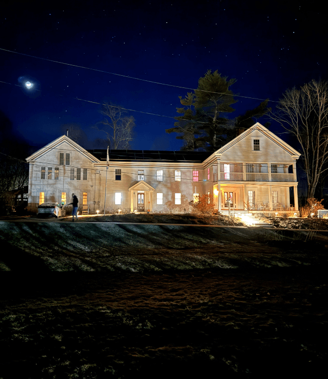 A well-lit white house under a starry night sky, with a person standing outside.