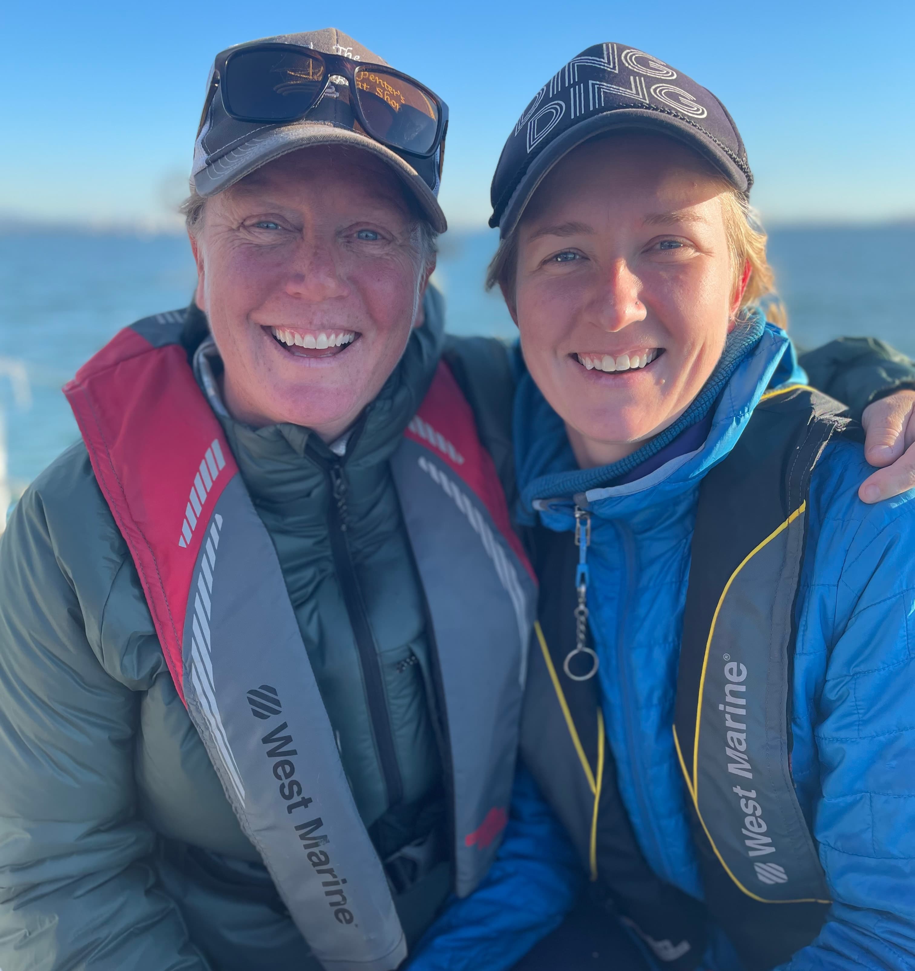 Two women wearing life jackets smile together on a boat with water in the background.