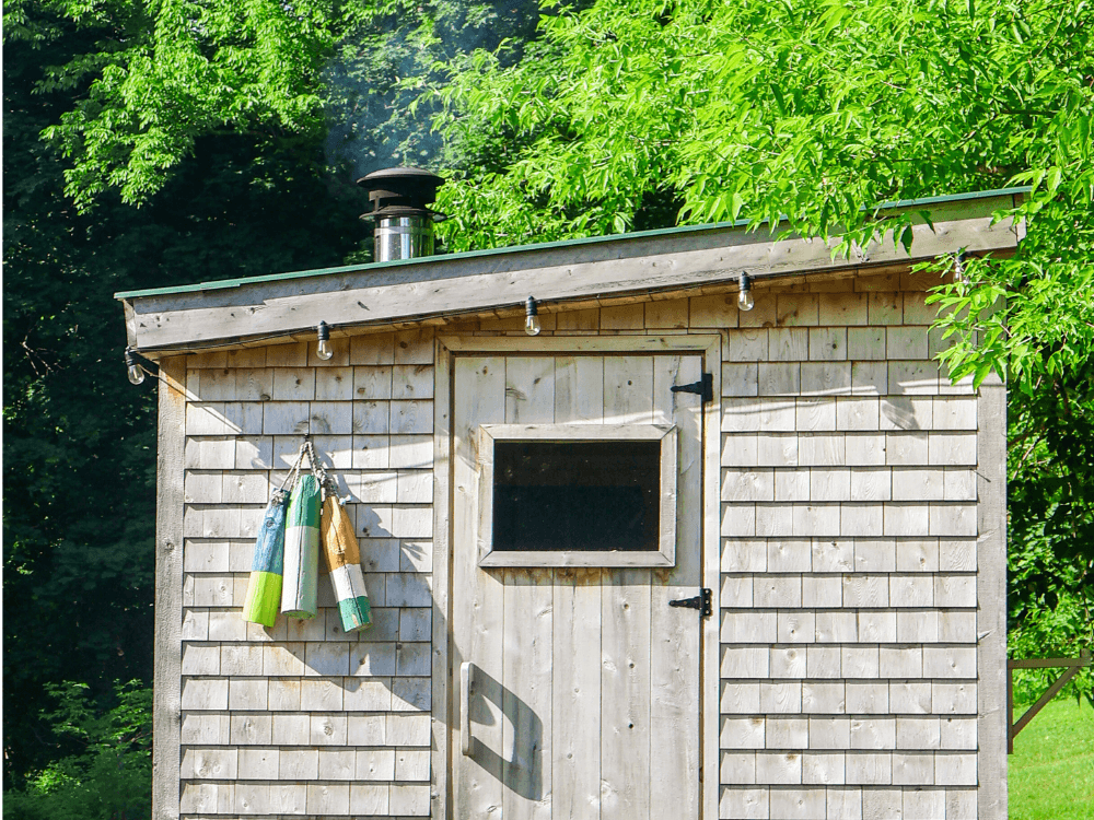 A wooden shed with a chimney, featuring colorful fishing buoys hanging from the door.